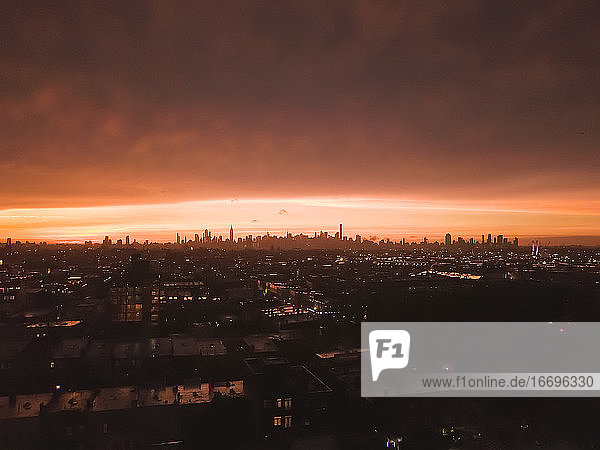 Luftaufnahme von Brooklyn über weit weg Manhattan Skyline in der Ferne nach Sonnenuntergang mit feuerrotem Licht und Wolkenkratzer Silhouette