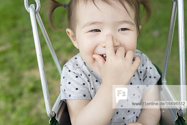 Adorable Baby Girl lächelt mit der Hand über dem Mund beim Schwingen im Freien