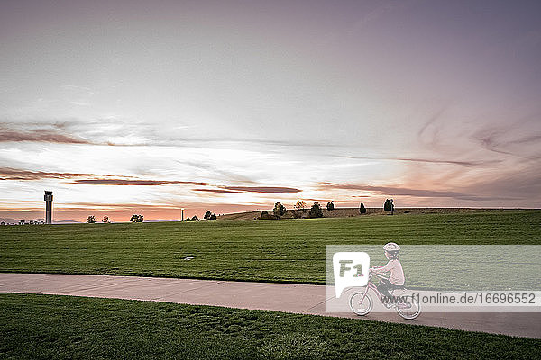 junges Mädchen radelt bei Sonnenuntergang in der Nähe eines grasbewachsenen Hügels