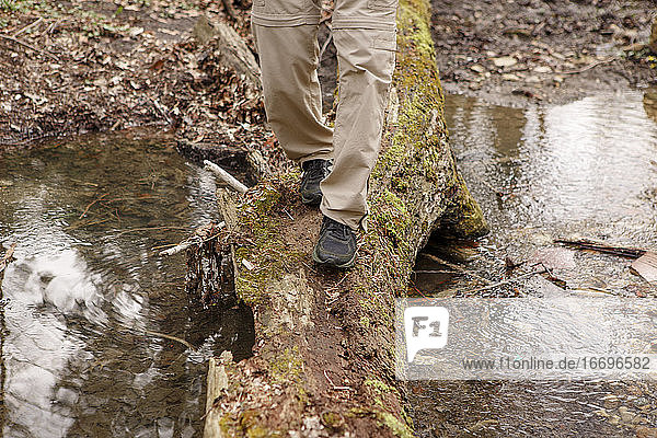 Bottom-half of a man crossing a creek on moss-covered log in nature