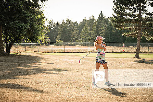 Sporty young girl with golf club standing on golf fairway