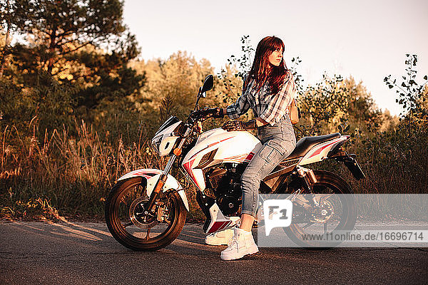 Confident woman sitting on motorcycle on country road looking back