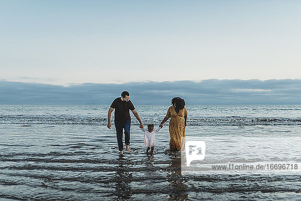 Landscape view of young family of three walking together in the ocean