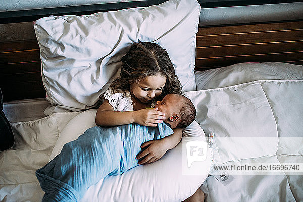 young girl holding newborn baby brother on bed