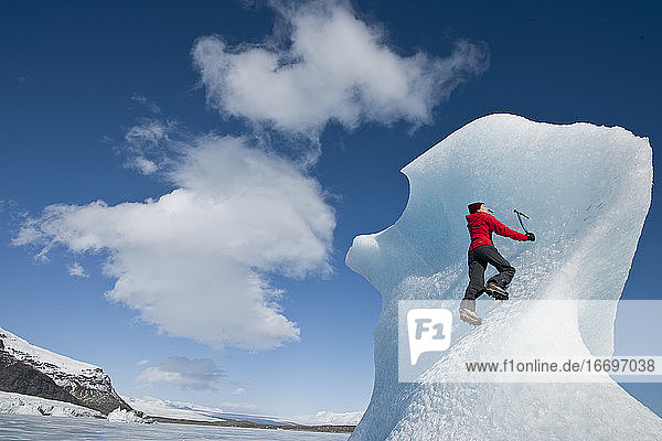 Frau klettert auf einen Eisberg in der Lagune des Fjallsjoull-Gletschers