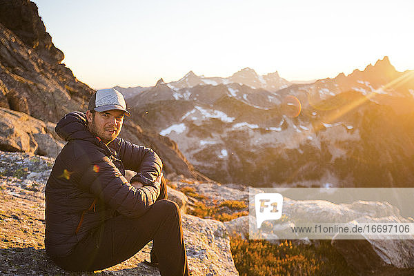 Portrait of man sitting on rock at sunset in mountains.