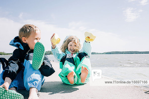Geschwister  die an einem windigen Tag am Strand lachend ihre Schuhe festhalten