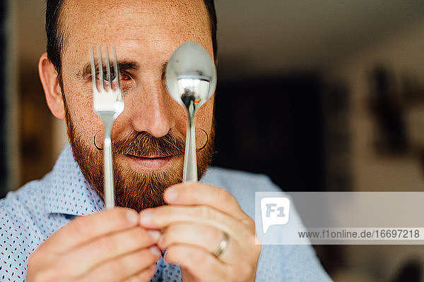 Close up portraits of man with moustache holding fork and spoon