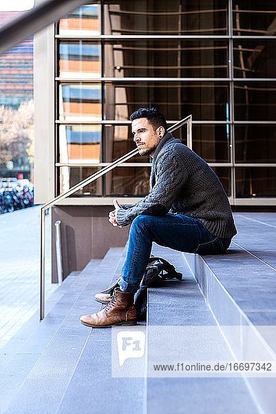 Junger Mann in Freizeitkleidung sitzt am Eingang eines Bürogebäudes