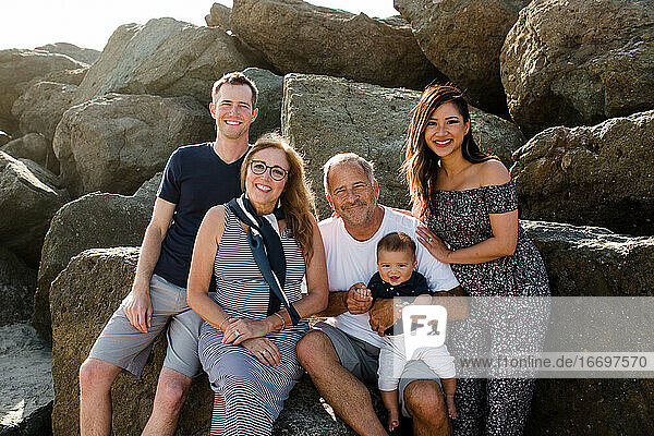 Family of Five Smiling for Camera Sitting on Rocks at Beach