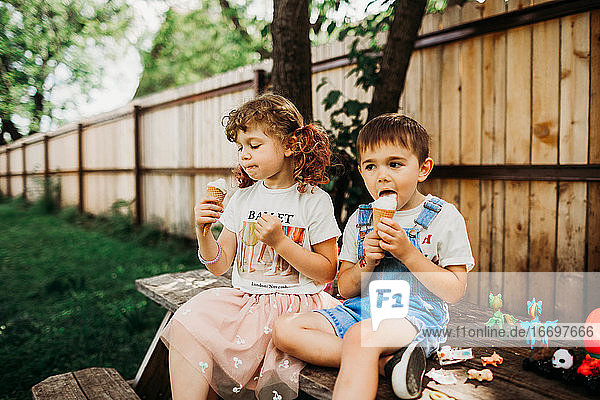 Kinder im Vorschulalter sitzen auf einem Picknicktisch und essen Eiswaffeln