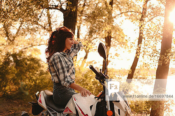 Glückliche junge Frau entspannt auf einem Motorrad sitzend inmitten von Bäumen