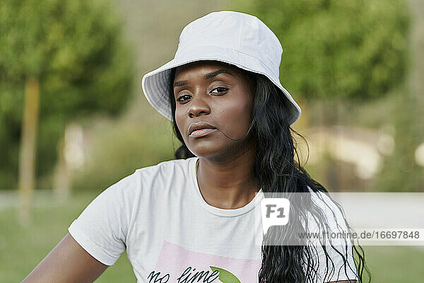 Schöne schwarze Frau mit weißer Mütze  die in einem Park in die Kamera schaut