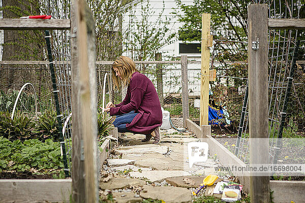 Eine Frau pflanzt Samen in ihrem Garten  während ein Kind im Hintergrund spielt