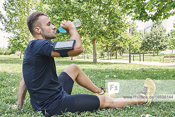 Mann trinkt nach dem Training ein Sportgetränk. Er befindet sich in einem Park im Freien.