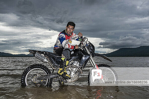 Mann posiert auf seinem Dirt-Bike in einem See bei Pak Chong / Thailand