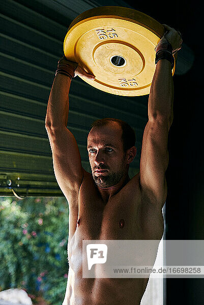 Hemdloser  fitter junger Mann beim Training mit einer Stahlscheibe in einer Garage