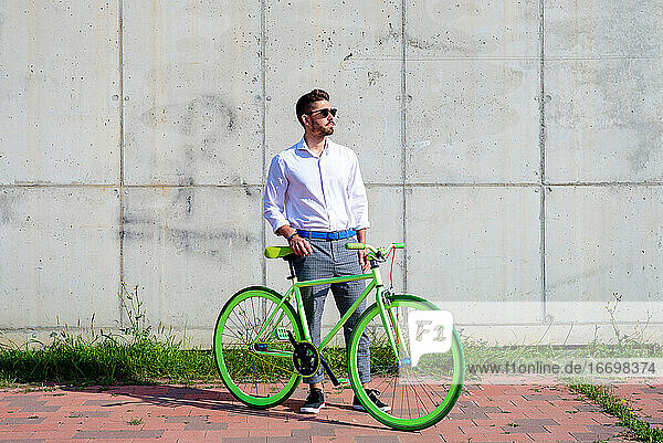 Junger bärtiger Mann mit Sonnenbrille steht mit Fahrrad im Freien