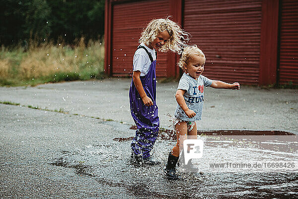 Siblings boy and girl jumping in a puddle having fun and smiling
