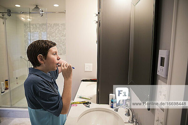 Teen Boy schaut in den Spiegel  während er sich im modernen Badezimmer die Zähne putzt