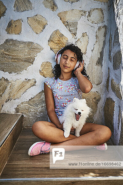 ein kleines Mädchen hört mit ihrem weißen Hund Musik