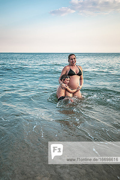 5 Jahre altes Kind  das seine schwangere Mutter umarmt  hüfttief im Meer