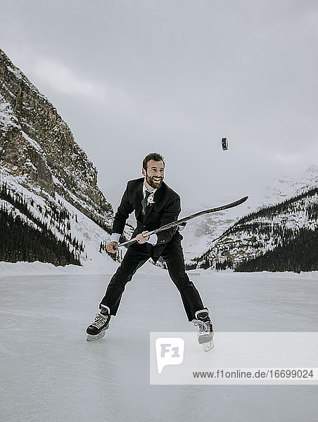 man in suit and ice skates juggles hockey puck on frozen Lake Louise