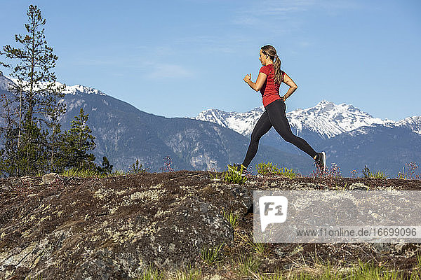 Seitenansicht einer starken Sportlerin  die beim Fitnesstraining auf dem Lande gegen einen verschneiten Bergkamm läuft