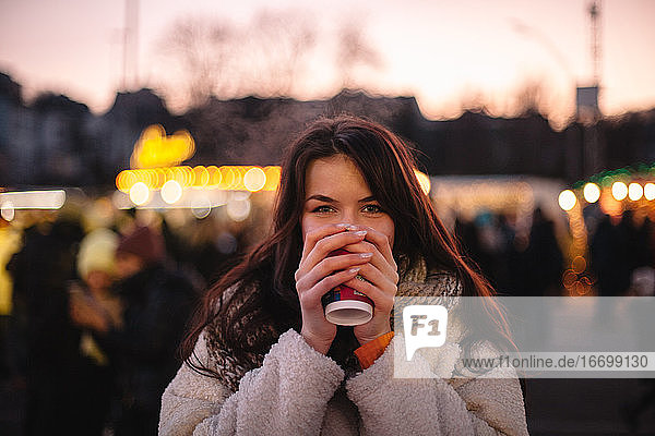 Glückliches Teenager-Mädchen trinkt Glühwein auf dem Weihnachtsmarkt in der Stadt