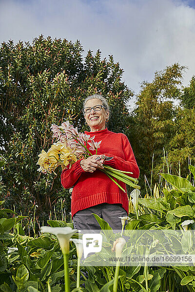 Frau im Ruhestand hält frisch geschnittene Blumen in ihrem Garten