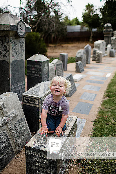 Zweijähriges Kind auf dem Grabstein sitzend und lächelnd