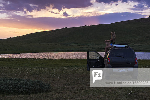 Frau sitzt auf einem Geländewagen  der bei Sonnenuntergang auf einem Feld geparkt ist
