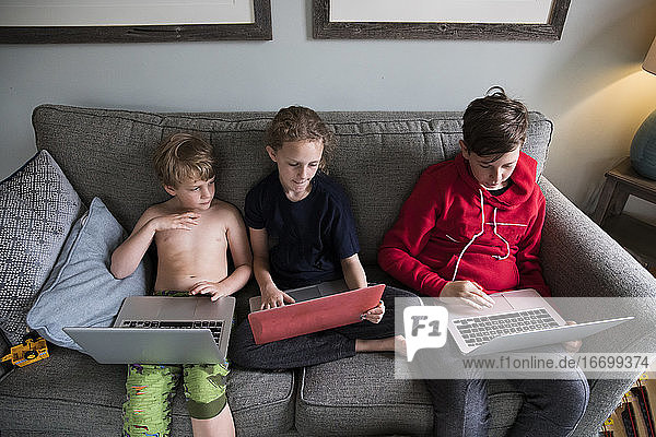 Drei Geschwister arbeiten gemeinsam an Laptops und lernen virtuell