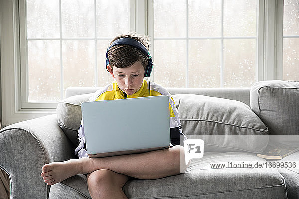 Junge im Teenageralter trägt Kopfhörer und arbeitet am Laptop für die virtuelle Schule