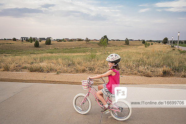 smiling young girl rides through a neighborhood park in the evening