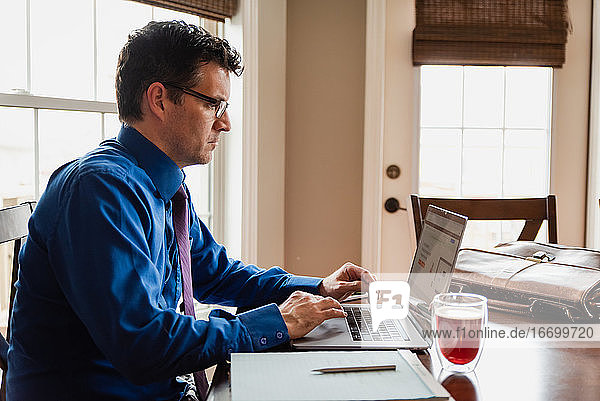 Man in shirt and tie working from home using computer at dining table.