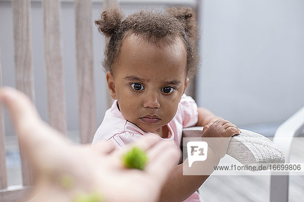 Ein weibliches Kleinkind starrt auf ein Stück Brokkoli