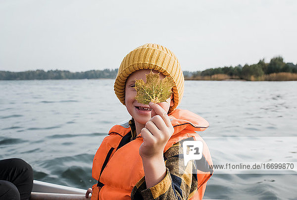 Junge auf einem Fischerboot  der ein Ahornblatt hochhält und sich freut