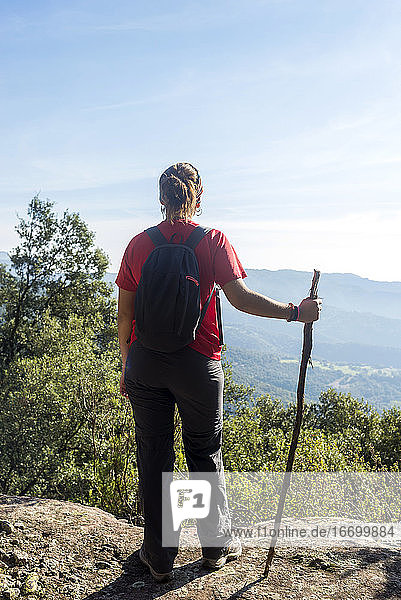 Rückansicht einer jungen Frau  die auf einem hohen Berg steht und einen Stock hält