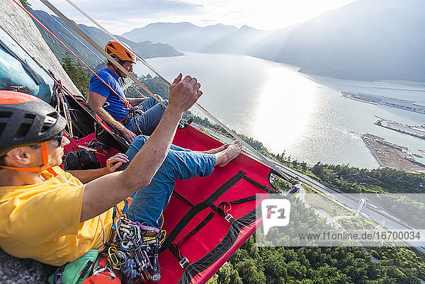 Two men sitting on a portaledge enjoying sunset and view in Squamish