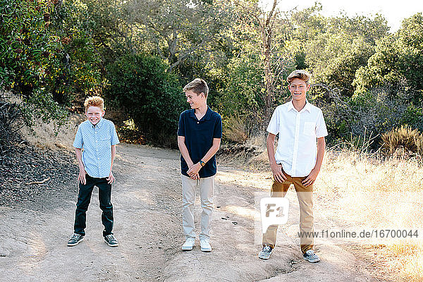 Three Young Brothers Stand Together Outside On a Trail Smiling
