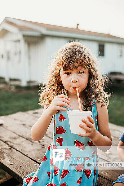 Close up of young girl drinking snow cone at table during sunset