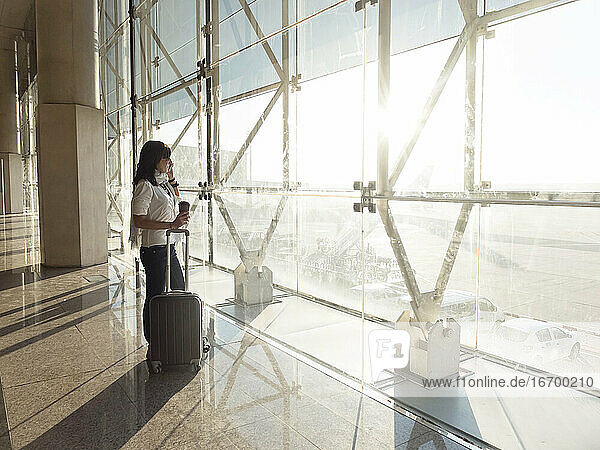 Junge Frau mit Koffer telefoniert beim Warten auf den Flug