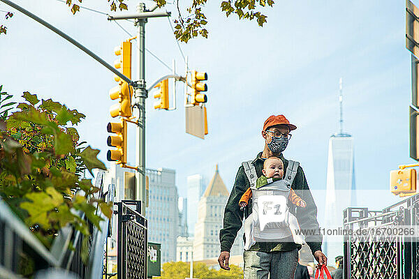 Vater trägt seine süße Tochter in der Babytrage beim Spaziergang in der Stadt während COVID-19