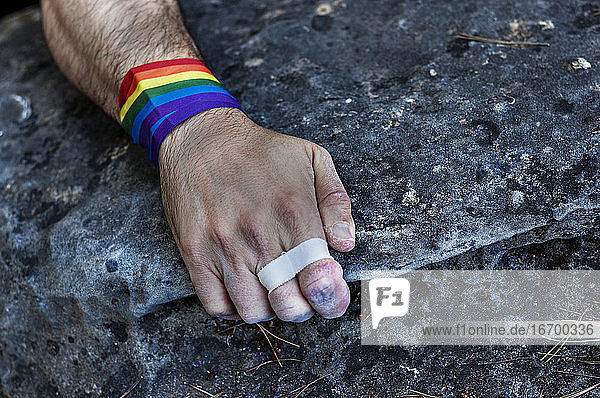Die Hand eines Bergsteigers mit einem schwulen Armband  das sich am Felsen festhält.