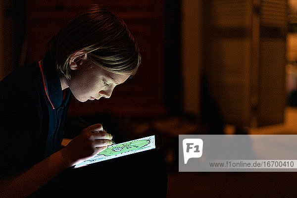 Profil eines Tween  das mit einem Stift auf einem Tablett in einem schwach beleuchteten Raum zeichnet