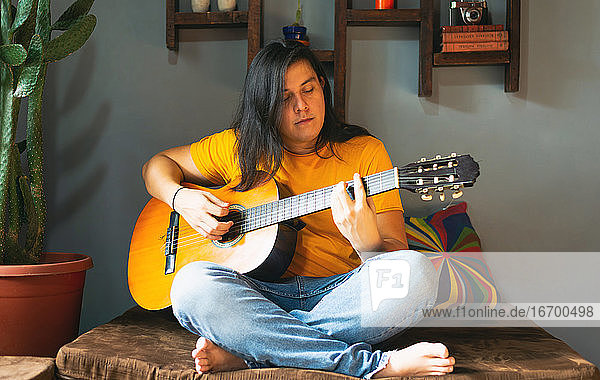Mann mit langen Haaren,  der während der Quarantäne zu Hause entspannt Gitarre spielt