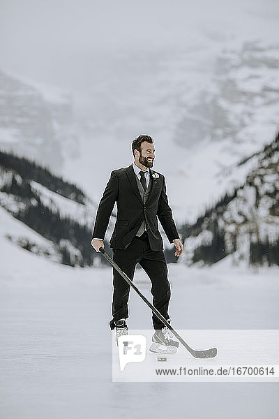 Man in black suit  hockey skates and hockey stick poses on frozen lake