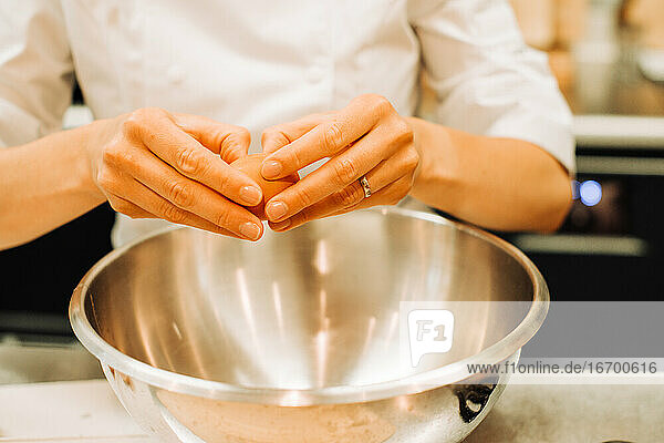 Weibliche Hände schlagen Eier in einer Metallschüssel in einer Restaurantküche auf