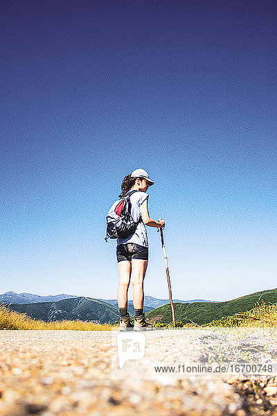 Frau wandert auf Straße gegen Berglandschaft und blauen Himmel